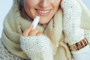 woman in roll neck sweater and cardigan using lip balm in winter.